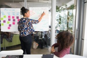 Two women collaborating on project strategy using notes in modern office.
